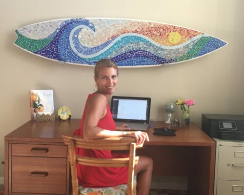 Betsy at a computer with a surfboard on the wall behind her
